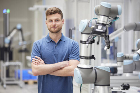 Confident technician with arms crossed standing next to machine in industry - RBF09071