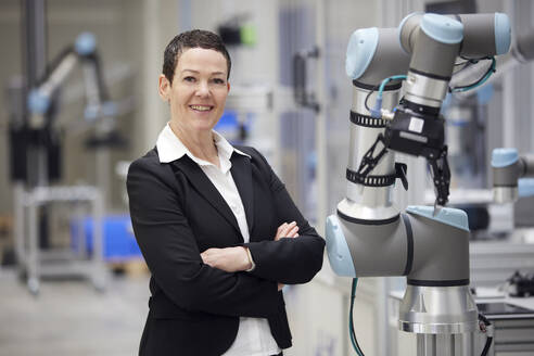 Confident smiling businesswoman standing with arms crossed in industry - RBF09075