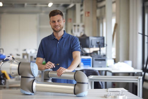 Smiling technician standing near robotic arm in industry - RBF09093