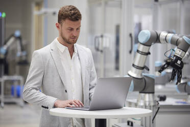 Geschäftsmann mit Laptop auf dem Tisch in einer modernen Fabrik - RBF09105