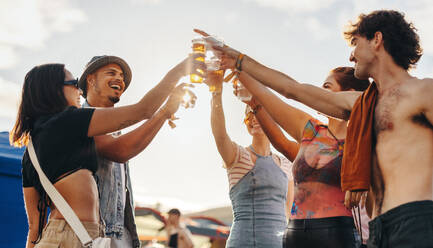 Group of friends gathers together, raising their beers in a celebratory toast, capturing the essence of festival fun and forging unforgettable memories of joy and camaraderie. This photo has intentional use of 35mm film grain. - JLPPF02181
