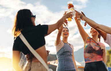 Happy friends raise their glasses in a toast, commemorating the arrival of summer and celebrating the lively atmosphere of a festival, fueled by refreshing beers. This photo has intentional use of 35mm film grain. - JLPPF02183