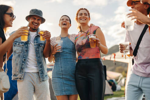Group of friends sharing heartfelt moments, laughter and chilled drinks in the spirited ambiance of a summer festival. Happy friends having fun together at a music festival. This photo has intentional use of 35mm film grain. - JLPPF02186