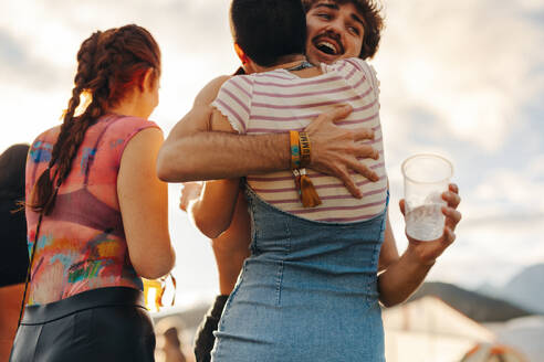 Friends excitedly embrace each other as they reunite at a thrilling summer festival, ready to immerse themselves in a world of fun and adventure. Young people meeting at a party. This photo has intentional use of 35mm film grain. - JLPPF02190