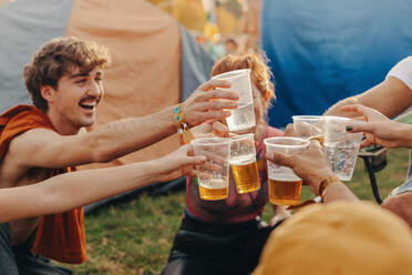 Happy friends sharing a moment of festival merriment with their beers raised in a joyous toast. Group of young people celebrating and having fun together at a festival camp. This photo has intentional use of 35mm film grain. - JLPPF02197