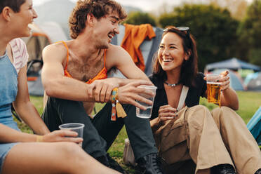 Happy young people savour the refreshing taste of cold beers while engaging in lively conversations, basking in the festive atmosphere of a delightful summer festival. This photo has intentional use of 35mm film grain. - JLPPF02207