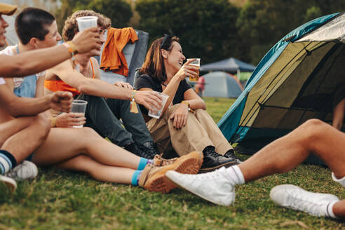 Group of friends raises their beer cups in celebration, capturing the essence of joy and camaraderie that permeates the summer music festival. Happy young people having fun at a camp. This photo has intentional use of 35mm film grain. - JLPPF02210