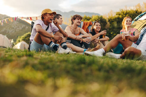 Vibrant group of young individuals gathers at the festival camp, engaging in lively conversations, enjoying refreshing beers, and creating a joyous atmosphere of celebration and camaraderie. This photo has intentional use of 35mm film grain. - JLPPF02213