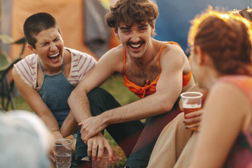 Carefree young people embrace the spirit of summer, laughing and drinking refreshing beers together at a festival party. Friends enjoying themselves at a youth music festival. This photo has intentional use of 35mm film grain. - JLPPF02215