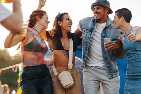 Friends groove to the rhythm and make unforgettable memories together at the lively summer music festival. Happy youngsters having fun and living their best lives at a party. This photo has intentional use of 35mm film grain. - JLPPF02220