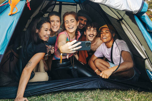 Eine Gruppe junger Freunde hält einen glücklichen Moment mit einem Selfie fest und bewahrt so ihre Campingerinnerungen und ihre starke Verbundenheit. Die absichtliche Verwendung von 35-mm-Filmkorn verstärkt das nostalgische Gefühl - JLPPF02224