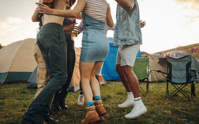 Youngsters dancing outside their festival tents, reveling in the vibrant energy and enjoying every exhilarating moment of the music festival experience. Group of friends celebrating at a summer camp. This photo has intentional use of 35mm film grain. - JLPPF02229