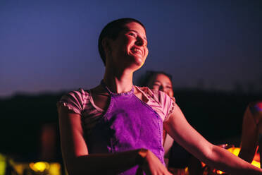 Joyful young woman gracefully dances, fully immersed in the mesmerizing music at a festival concert. Happy young woman having the night of her life at a fun summer festival. This photo has intentional use of 35mm film grain. - JLPPF02240