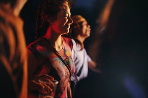 Woman lets loose and dances with joy, fully embracing the energetic atmosphere of a lively summer music festival. Happy young woman having fun at a crowded night party. This photo has intentional use of 35mm film grain. - JLPPF02241