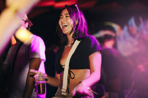 Vibrant young woman unleashes her inner dancer, moving to the pulsating beats and lively ambiance of a music festival. Happy young woman having fun at a summer night party. This photo has intentional use of 35mm film grain. - JLPPF02245