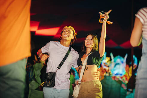 Young couple immerses themselves in the vibrant festival atmosphere, celebrating and partying to the infectious music, creating unforgettable memories of pure joy and togetherness. This photo has intentional use of 35mm film grain. - JLPPF02246