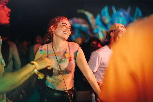 Woman joins a lively group of young people in embracing the exhilarating energy of a musical concert and creating unforgettable moments of fun and togetherness. Woman enjoying a summer party. This photo has intentional use of 35mm film grain. - JLPPF02251