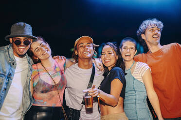 Group of young friends having fun together at a musical concert, reveling in the joy and excitement of the moment. Happy young people having a good time in the vibrant festival nightlife. This photo has intentional use of 35mm film grain. - JLPPF02252