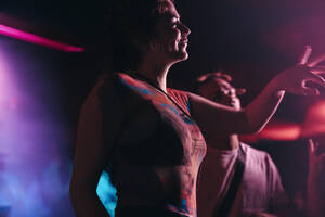 Young woman enjoying herself in the vibrant energy of a music festival, dancing with her friends and celebrating summer with enthusiasm. Female festival goer having fun at night. This photo has intentional use of 35mm film grain. - JLPPF02258