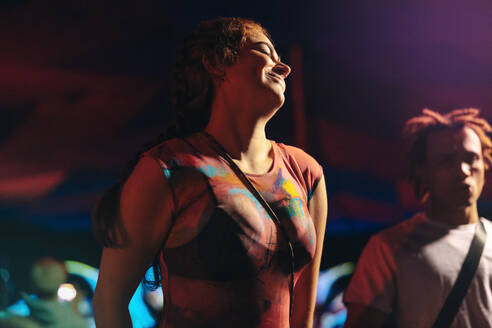 Woman embraces the night at a music concert, dancing and enjoying herself in the vibrant atmosphere. Young woman creating unforgettable moments of celebration at a festival. This photo has intentional use of 35mm film grain. - JLPPF02259