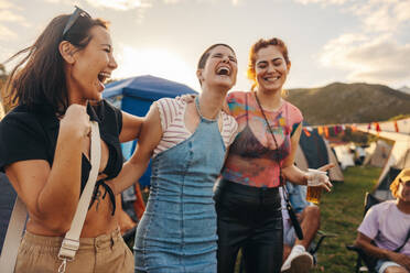 Three girlfriends embrace, laugh, and celebrate the magic of the summer music festival, cherishing the bond of friendship and creating lasting memories in the midst of the lively event. This photo has intentional use of 35mm film grain. - JLPPF02264
