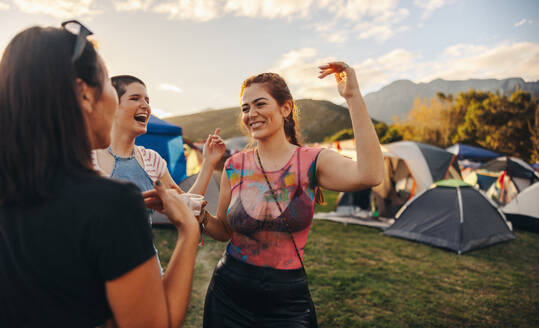 Group of happy young women dances and celebrates together, immersing themselves in the infectious energy and excitement in a vibrant festival atmosphere. This photo has intentional use of 35mm film grain. - JLPPF02268