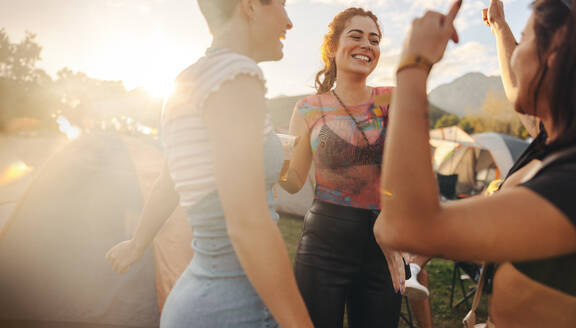 Lively group of young people fully embraces the spirit of a summer music festival. They dance together, celebrating their friendships with happiness amidst the vibrant atmosphere. This photo has intentional use of 35mm film grain. - JLPPF02269