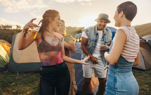 Group of young people and friends have fun in a summer music festival. As the sun sets, they dance together, savoring the moment, and sharing drinks in a celebration of the joyful day. This photo has intentional use of 35mm film grain. - JLPPF02271