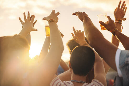 Excited crowd raises their hands in bliss, embracing the collective joy and excitement from a music festival. Group of young people having fun at a summer concert. This photo has intentional use of 35mm film grain. - JLPPF02279