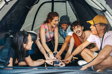 Group of happy festival goers gathers in a tent, engaging in a fun-filled drinking game, adding to the joyful ambiance of the festival atmosphere. This photo has intentional use of 35mm film grain. - JLPPF02282
