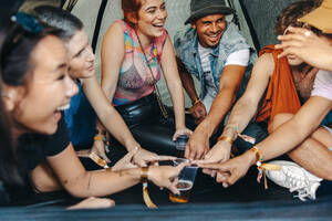 Young people fully embrace the energetic summer festival vibes as they gather for a delightful camping experience. Under a tent, they engage in a spirited drinking game, celebrating the festival spirit with laughter. This photo has intentional use of 35mm film grain. - JLPPF02283