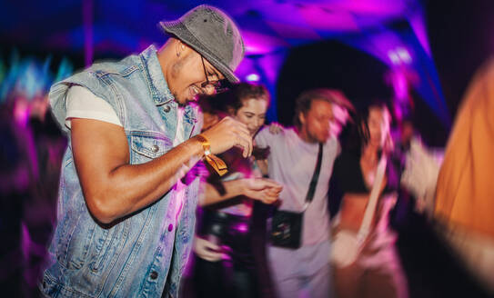 Young people dance in sync to the beat under the vibrant nighttime ambiance, enjoying themselves in the rhythmic grooves of a summer music festival. This photo has intentional use of 35mm film grain. - JLPPF02284