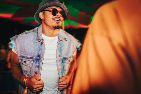 Young man showcases his dance skills at a vibrant nighttime party, fully immersed in the pulsating energy and excitement of a vibrant music festival. This photo has intentional use of 35mm film grain. - JLPPF02285