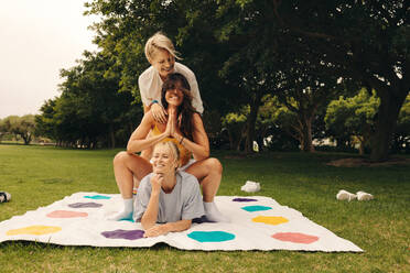 Three friends having fun while playing a mat game in a park. Group of women smiling and laughing together, enjoying outdoor leisure activities in summer. This photo has intentional use of 35mm film grain. - JLPPF02291
