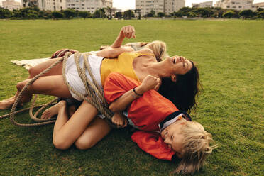 Women engage in playful rope escape on the park lawn. Group of friends laughing and having fun together, enjoying genuine friendship vibes outdoors. This photo has intentional use of 35mm film grain. - JLPPF02294