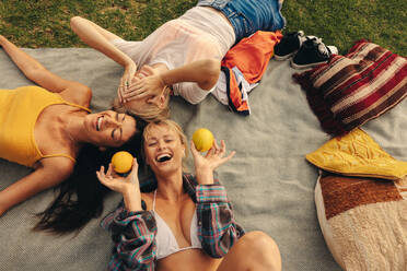 Top view of female friends, relaxed and carefree, lying in a park enjoying the vibrant summer day together. Mature women having fun outdoors, laughing happily as they celebrate friendship. This photo features intentional film grain for artistic effect. - JLPPF02296