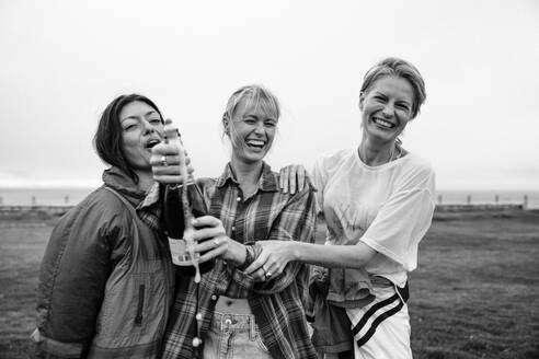 Happy friends pop a champagne bottle outdoors, celebrating and having fun together. Group of women laughing with joy in an authentic moment of friendship. This photo has intentional use of 35mm film grain. - JLPPF02301