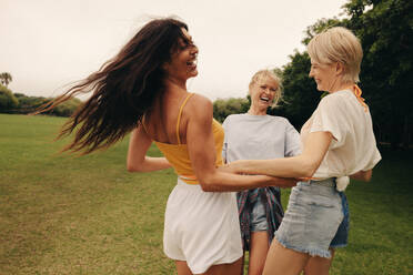 Group of female friends is playing with a hula hoop outdoors on a sunny day in the park. They are having fun, laughing, and bonding while enjoying a leisure activity together. This photo has intentional use of 35mm film grain. - JLPPF02313