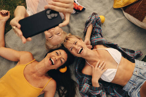 A group of 30-something women enjoy each other's company outdoors, capturing their joy and friendship in a playful selfie with film grain - JLPPF02319