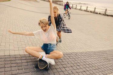 Two female best friends having fun at the promenade, celebrating and enjoying the summer day with playful skating and socializing. Casual clothing, real smiles, and happy memories. This photo has intentional use of 35mm film grain. - JLPPF02320