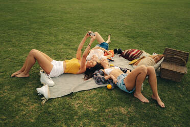 Drei Freunde machen ein Picknick und halten glückliche Momente mit einem Selfie fest. Sie genießen das warme Wetter und den Filmkorn-Effekt - JLPPF02333