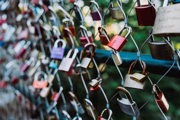 Bunch of various love padlocks hanging on net fence on blurred background of green park - ADSF44549