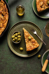 Top view of slice baked Italian focaccia bread with green olives in plate on dining table with drink on green background - ADSF44555