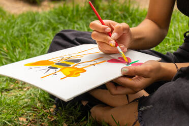 Anonymous female artist using brush while painting butterfly on white paper sheet with green liquid - ADSF44557