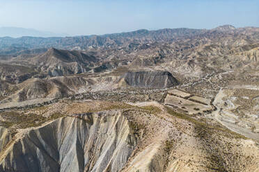 Aerial view of rough rocky mountains with dry river meandering through dry grass barren terrain with no habitation and trees in arid region - ADSF44589