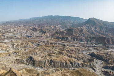 Aerial view of rough rugged mounts with uneven surface forming natural valley and dry river flowing through under blue sky in daylight - ADSF44591