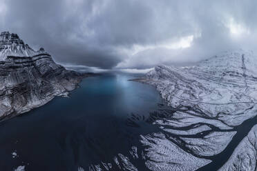 Aerial view of sea water surrounded by snowy mountains under cloudy sky on winter day in Iceland - ADSF44596
