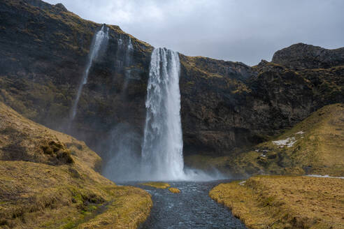 Scenic view of Seljalandsfoss waterfall falling from rough rocky cliff into river down rocks in mountainous woods in Iceland - ADSF44603