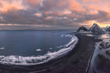 Drone view of sea waves washing coast with foamy water surrounded by snowy mountains under bright sky during sunset in Iceland - ADSF44607