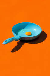 Whole raw egg yolk placed in blue frying pan with handle isolated against orange background - ADSF44636
